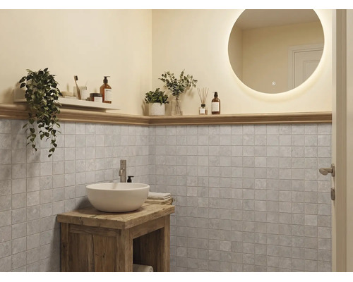 Salle de bains moderne avec miroir rond éclairé, vasque blanche sur meuble en bois rustique et carrelage mural carré gris.