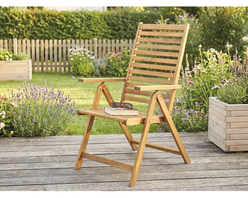 Fauteuil de jardin pliant en bois sur une terrasse en bois dans un jardin lumineux avec des plantes et une clôture.