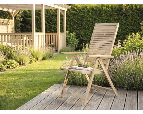Klappbarer Gartenstuhl aus Holz mit Armlehnen auf einer Holzterrasse in einem hellen, gepflegten Garten.