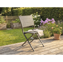Chaise de jardin pliante avec structure en métal et revêtement en textile sur une terrasse en bois dans un jardin ensoleillé avec des fleurs.