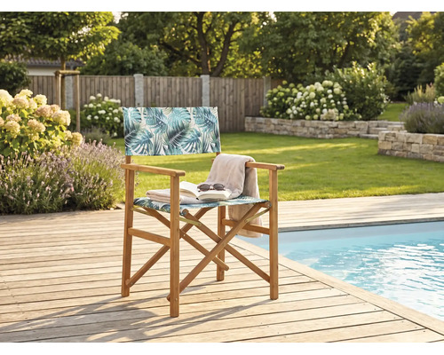 Chaise de metteur en scène en bois avec motif de feuilles de palmier sur une terrasse en bois à côté d'une piscine dans un jardin.