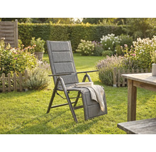 Fauteuil de jardin à dossier haut rembourré avec repose-pieds réglable dans un jardin lumineux avec pelouse, fleurs et table en bois.