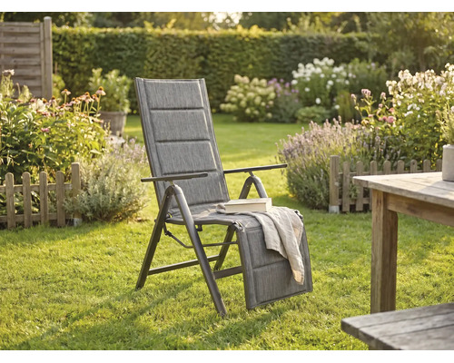 Fauteuil de jardin à dossier haut rembourré avec repose-pieds réglable dans un jardin lumineux avec pelouse, fleurs et table en bois.