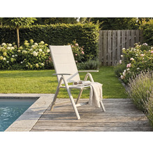 Chaise de jardin pliante moderne avec dossier haut sur une terrasse en bois au bord d'une piscine, entourée d'un jardin avec des fleurs.
