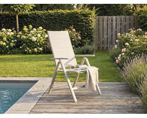 Chaise de jardin pliante moderne avec dossier haut sur une terrasse en bois au bord d'une piscine, entourée d'un jardin avec des fleurs.