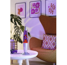 Lampe à lave moderne sur une table ronde dans un salon avec fauteuil, plante et tableaux muraux encadrés dans un éclairage d'ambiance.