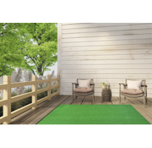 Tapis de gazon synthétique vert sur une terrasse en bois clair avec deux chaises de jardin et une clôture en bois en arrière-plan.