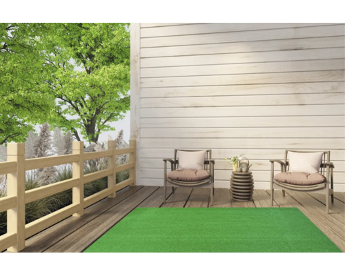 Tapis de gazon synthétique vert sur une terrasse en bois clair avec deux chaises de jardin et une clôture en bois en arrière-plan.