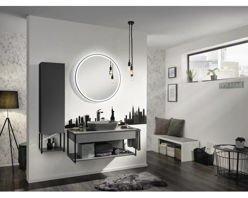 Salle de bains moderne avec miroir LED rond, meuble sous vasque gris, vasque à poser, colonne, sticker mural skyline et éclairage industriel.