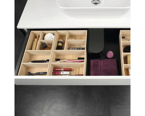 Tiroir de meuble sous-vasque de salle de bains organisé avec des séparateurs en bois contenant des articles de toilette, des brosses et une serviette.