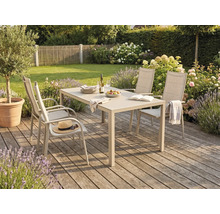 Salon de jardin comprenant une table rectangulaire et quatre chaises à dossier haut sur une terrasse en bois dans un jardin spacieux et fleuri.