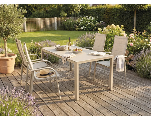 Salon de jardin comprenant une table rectangulaire et quatre chaises à dossier haut sur une terrasse en bois dans un jardin spacieux et fleuri.