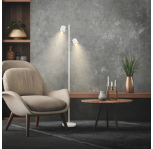 Salon moderne avec lampadaire blanc à deux projecteurs orientables, fauteuil beige et table d'appoint ronde en bois.