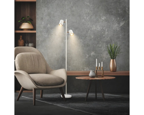 Salon moderne avec lampadaire blanc à deux projecteurs orientables, fauteuil beige et table d'appoint ronde en bois.