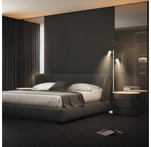 Chambre à coucher moderne avec un lit capitonné gris foncé, du linge de lit blanc et un lampadaire blanc fin à deux spots.