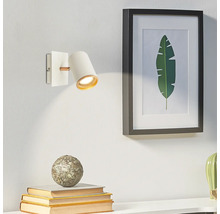 Applique murale moderne blanche en métal et bois avec projecteur cylindrique et intérieur doré à côté d'un tableau.