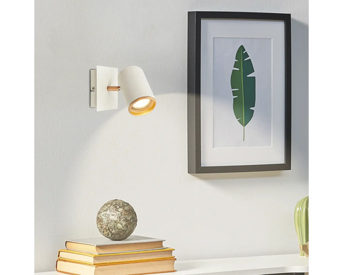 Applique murale moderne blanche en métal et bois avec projecteur cylindrique et intérieur doré à côté d'un tableau.