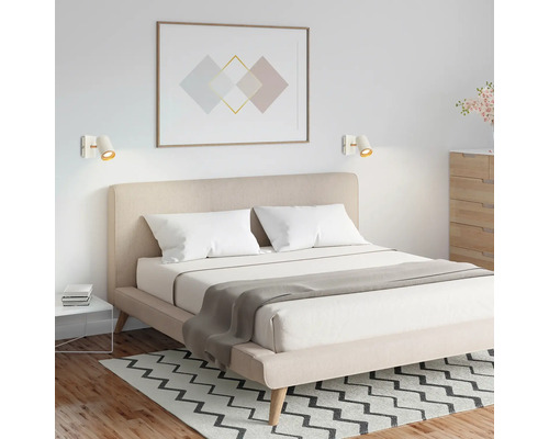 Chambre à coucher moderne avec lit double, tête de lit rembourrée beige et deux appliques murales blanches au-dessus du lit.