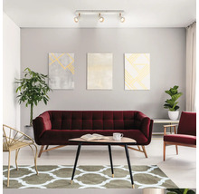 Salon moderne avec canapé en velours rouge, table basse en bois, tapis à motifs, plantes d intérieur et plafonnier à trois spots réglables.