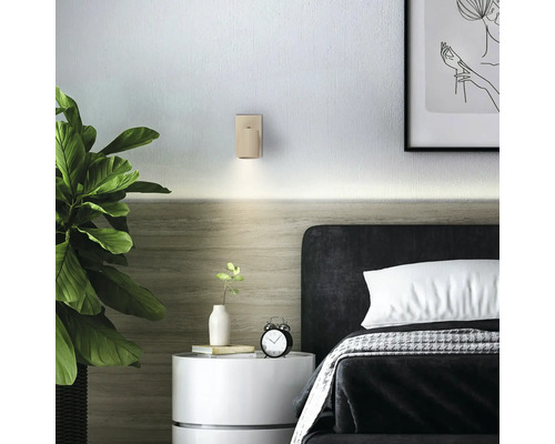 Applique murale beige à surface nervurée dans une chambre à coucher au-dessus d'une table de chevet blanche à côté d'un lit sombre.