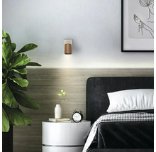 Chambre moderne avec applique murale en bois au-dessus d'une tête de lit sombre, table de chevet blanche avec réveil et grande plante verte.