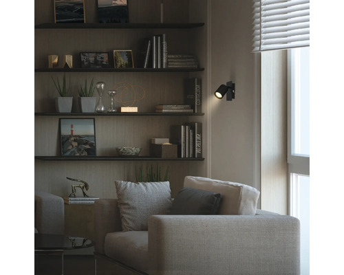 Salon moderne avec canapé en tissu et étagères murales. Un spot mural LED noir orientable crée un point lumineux dans la pièce sombre.