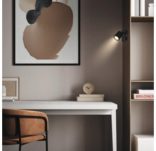 Spot mural LED noir fixé sur une étagère en bois au-dessus d'un bureau clair dans un bureau au design moderne.
