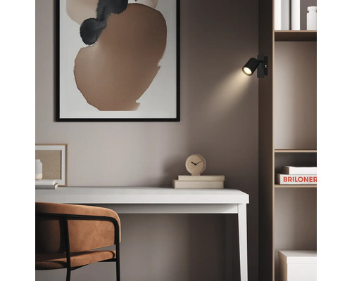 Spot mural LED noir fixé sur une étagère en bois au-dessus d'un bureau clair dans un bureau au design moderne.