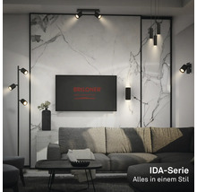 Salon moderne avec divers luminaires noirs de la série Briloner IDA, tels que lampadaire, applique et suspension devant un mur en marbre.
