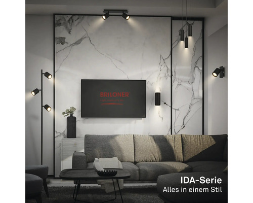 Salon moderne avec divers luminaires noirs de la série Briloner IDA, tels que lampadaire, applique et suspension devant un mur en marbre.