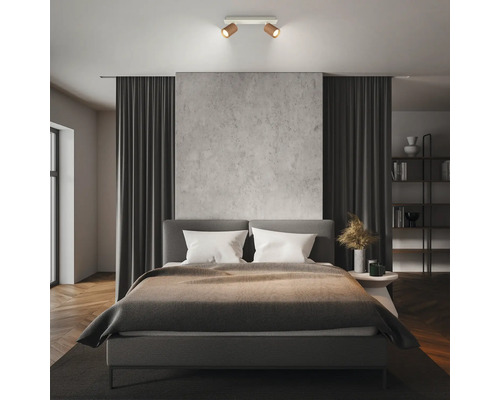 Spot de plafond moderne à 2 lampes en aspect bois au-dessus d'un lit double dans une chambre à coucher au design minimaliste.