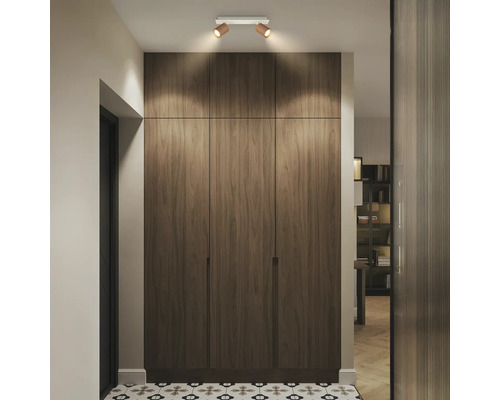 Spot de plafond orientable à deux lampes éclairant une armoire en bois sur toute la hauteur dans un couloir moderne avec sol carrelé.