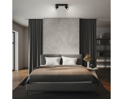 Spot de plafond noir moderne à deux lampes dans une chambre organisée avec mur en béton et lit gris.