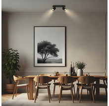 Salle à manger moderne avec table en bois, chaises et plante. Un plafonnier noir à deux spots éclaire un tableau encadré au mur.