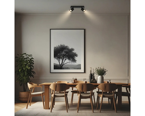 Salle à manger moderne avec table en bois, chaises et plante. Un plafonnier noir à deux spots éclaire un tableau encadré au mur.