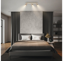 Plafonnier moderne avec trois spots dans une chambre lumineuse et organisée avec lit double, rideaux et mur texturé.