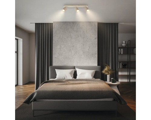Plafonnier moderne avec trois spots dans une chambre lumineuse et organisée avec lit double, rideaux et mur texturé.