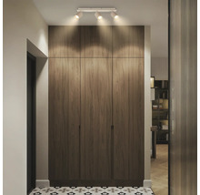 Plafonnier à trois spots éclairant une armoire encastrée aspect bois dans un couloir avec du carrelage à motifs, moderne et organisé.