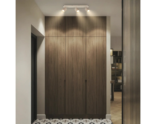 Plafonnier à trois spots éclairant une armoire encastrée aspect bois dans un couloir avec du carrelage à motifs, moderne et organisé.