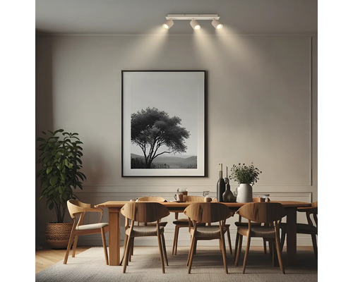 Salle à manger moderne avec table en bois, chaises et spot de plafond blanc à trois lampes éclairant un tableau au mur.