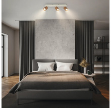Plafonnier à trois spots orientables dans une chambre moderne avec lit rembourré gris et rideaux sombres.