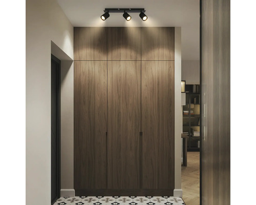 Couloir moderne avec un grand placard encastré à l'aspect bois, éclairé par un spot de plafond à trois lampes sur un sol carrelé à motifs.