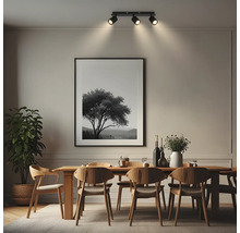 Plafonnier à trois spots dans une salle à manger moderne au-dessus d'une table en bois avec des chaises et un grand tableau.