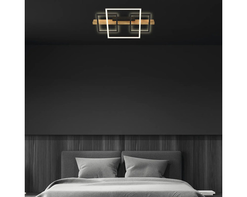 Plafonnier LED à trois éléments carrés et barre en bois dans une chambre à coucher moderne avec des murs sombres.