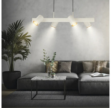 Salon moderne avec suspension blanche à quatre spots, canapé d'angle gris, table basse en marbre et grand palmier d'intérieur.