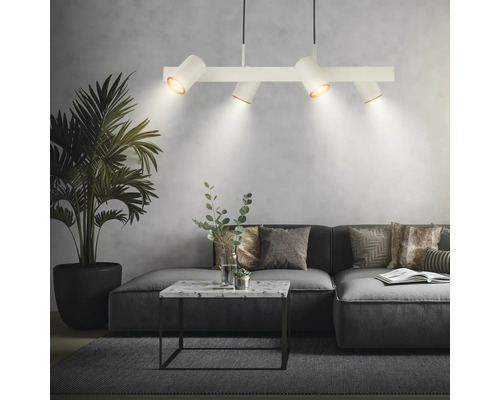 Salon moderne avec suspension blanche à quatre spots, canapé d'angle gris, table basse en marbre et grand palmier d'intérieur.