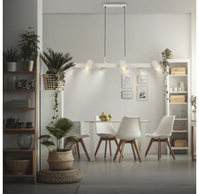 Salle à manger moderne et lumineuse avec une suspension à six lampes au-dessus d'une table avec quatre chaises, des étagères et des plantes d'intérieur.