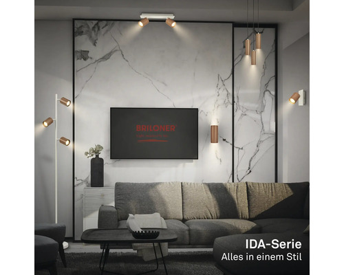Salon moderne et lumineux avec Briloner Logo sur la télévision, luminaires série IDA sur mur en marbre, plafond et lampadaire près du canapé.