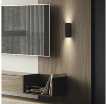 Applique murale cylindrique noire moderne diffusant vers le haut et le bas, fixée sur un panneau en bois dans un salon.