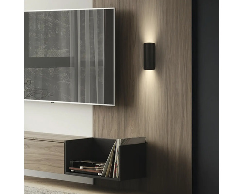 Applique murale cylindrique noire moderne diffusant vers le haut et le bas, fixée sur un panneau en bois dans un salon.